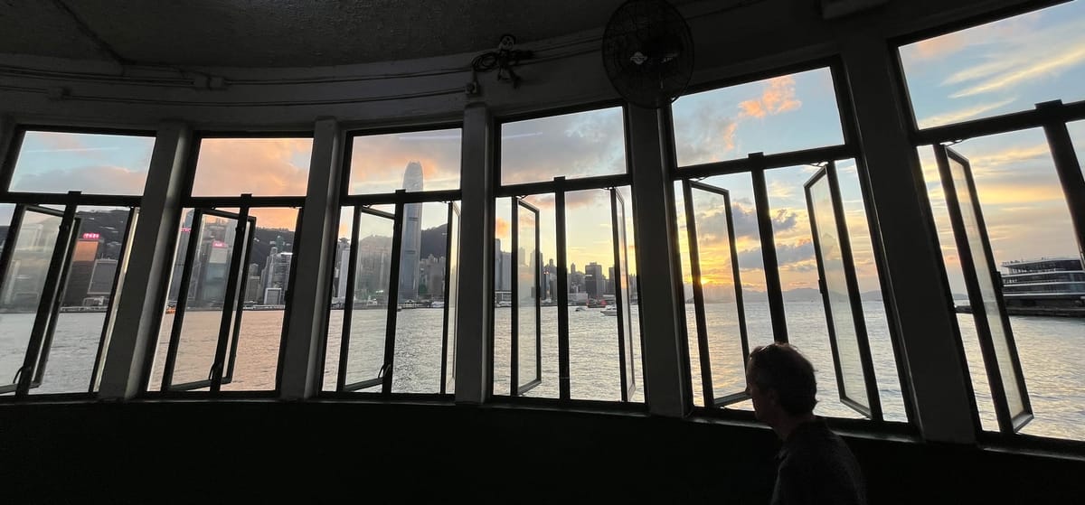 Panorama of sun setting behind the Hong Kong Island skyline, viewed through the windows of the TST Star Ferry Pier.